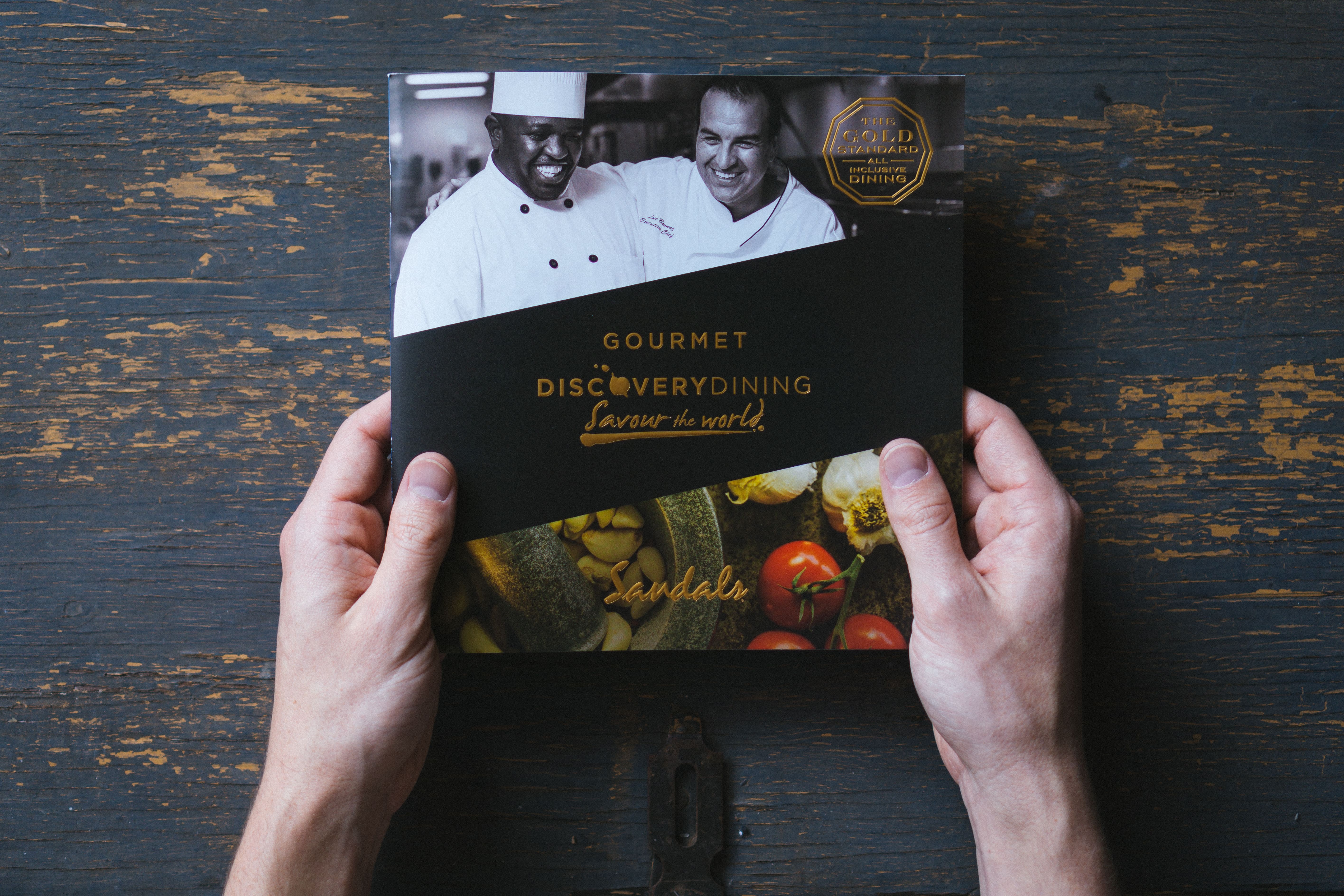 The cover of a menu book for Sandals Resorts reading Gourmet Discovery Dining, Savour the World.