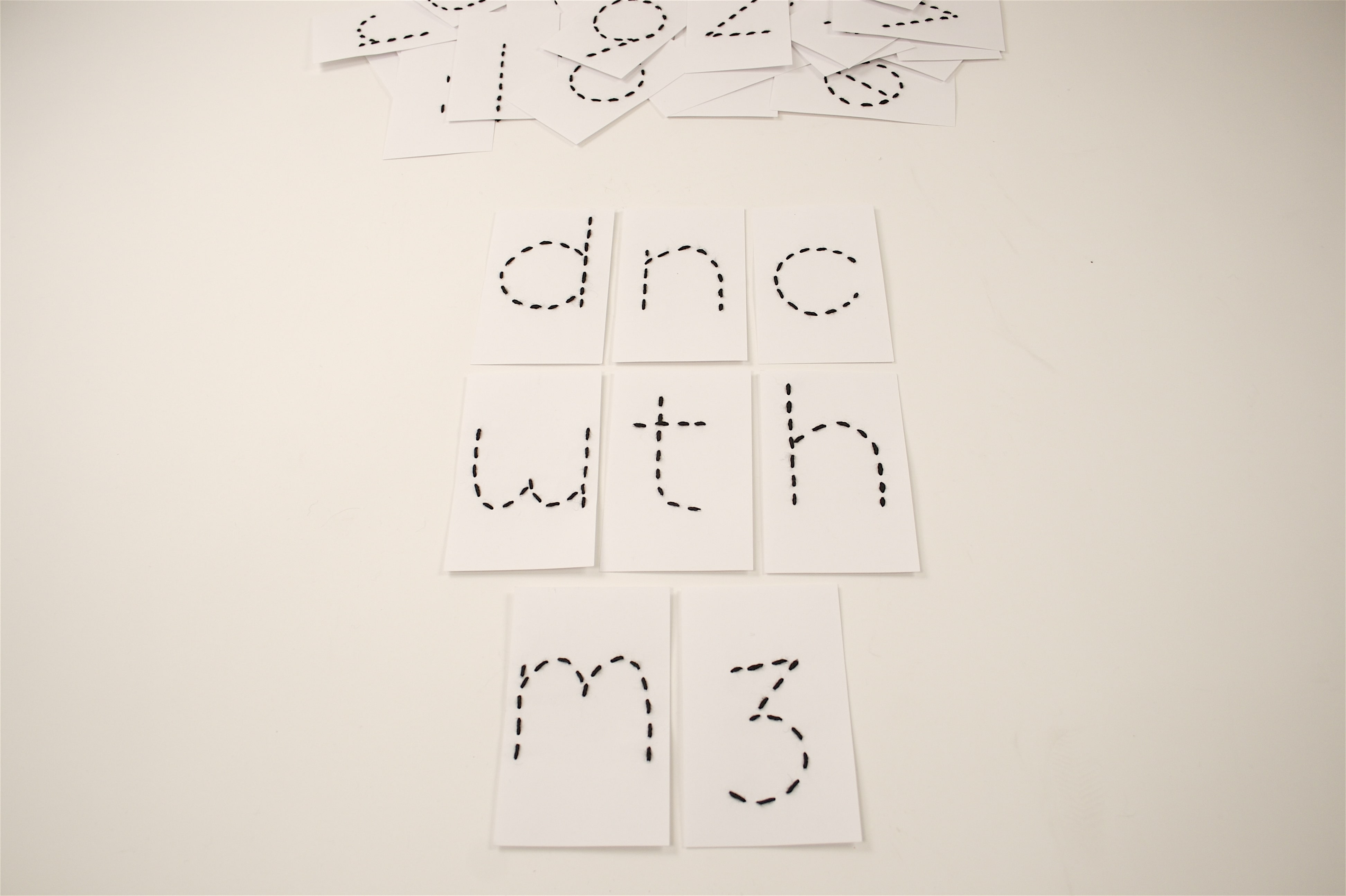 A series of white index cards, each with black yard letters threaded to spell out an abbreviation for 'dance with me'.
